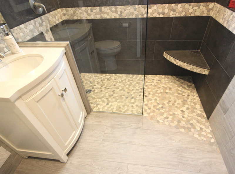 Bathroom with curbless walk-in shower with pebble transition detail on the shower edge, curved floting corner bench and pebble mosaic accent strip on the walls in Carleton Place by Renovation to Perfection.