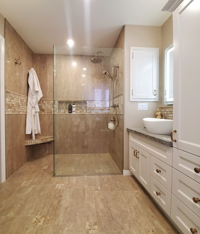 Bathroom with curbless, walk-in, linear drain shower with heated curved corner bench, basketweave travertine mosaic accent detail on the shower walls running through the niche. Travertine mosaic details incorporated to the floor pattern, concrete countertop on the vanity cabinet in Almonte by Renovation to Perfection.