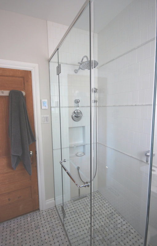 Custom shower with designer layout of subway tiles and marbe pencil strips on the walls, niche centered on the shower set, curbless basketweave mosaic floor in Renfrew by Renovation to Perfection.