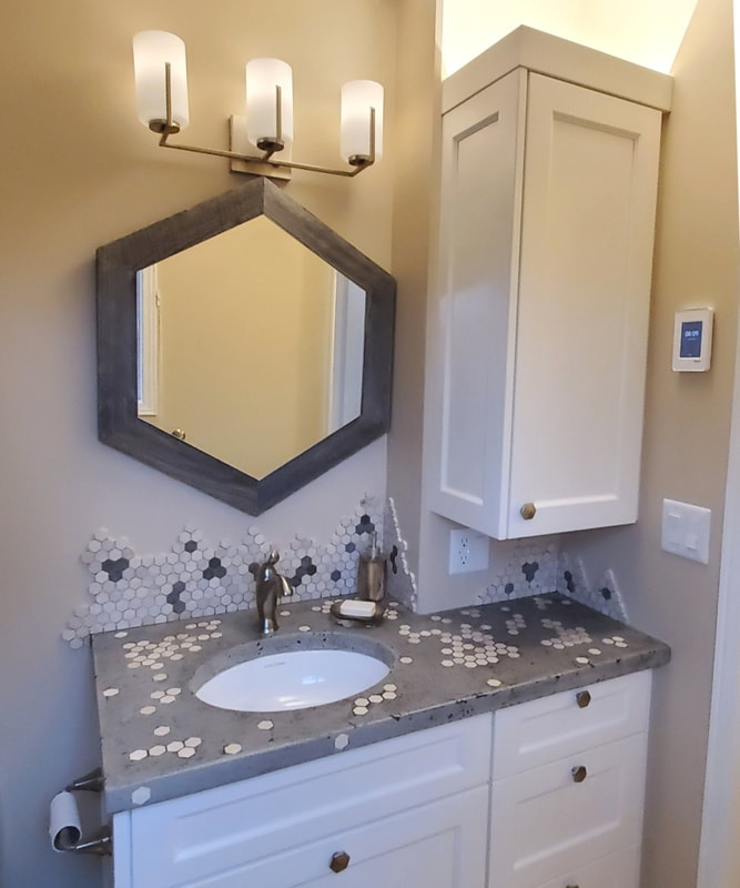 Tessalating bathroom - vanity detail with custom concrete countertop with embedded hex marble tiles and organic shape countertop with the same mosaic, hex shape mirror and LED light behind the cabinet crown for assent lighting in Almonte by Renovation to Perfection.