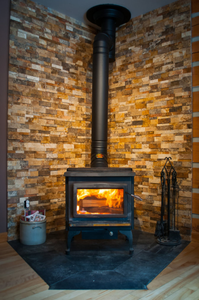 Woodstove corner with porcelain tile installed flush with the maple hardwood and stone mosaic on the walls in Almonte by Renovation to Perfection.